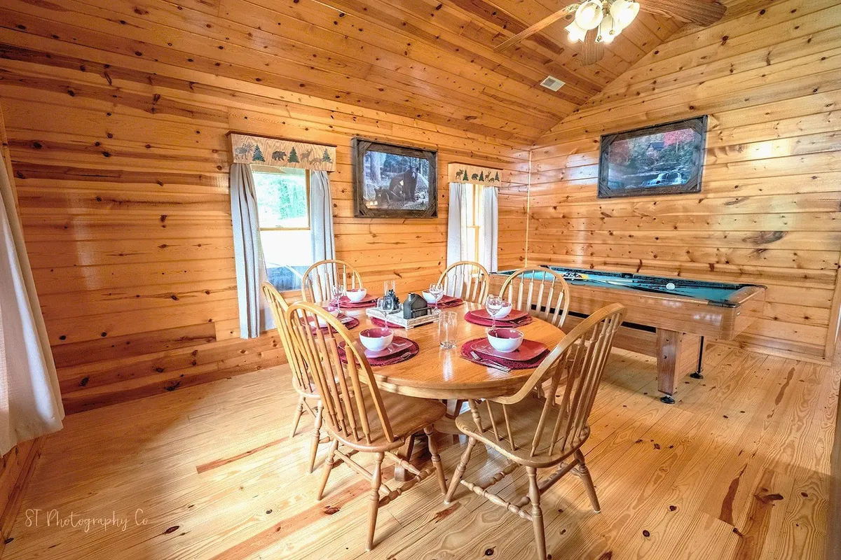 In this image, a dining table is set for a meal just steps from a pool table, all framed by rustic wooden walls. The mood is warm and welcoming, inviting families or friends to connect over food and games.