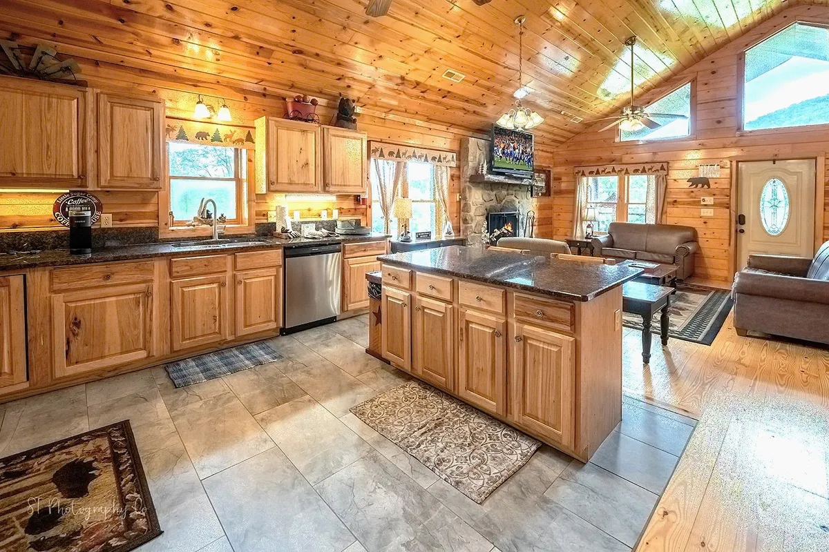 An open kitchen and living area with a prominent fireplace, kitchen island, and multiple seating options. Large windows let in natural light, reinforcing a connection to the outdoors and providing space for entertaining.