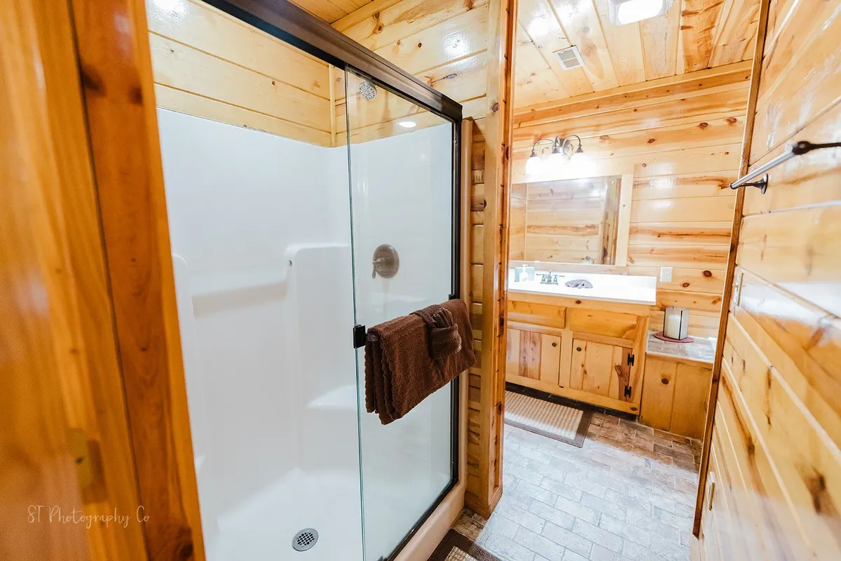 A spacious bathroom with a glass shower enclosure, wooden cabinetry, a large mirror, and a towel rack, all bathed in calm lighting for a relaxing feel.
