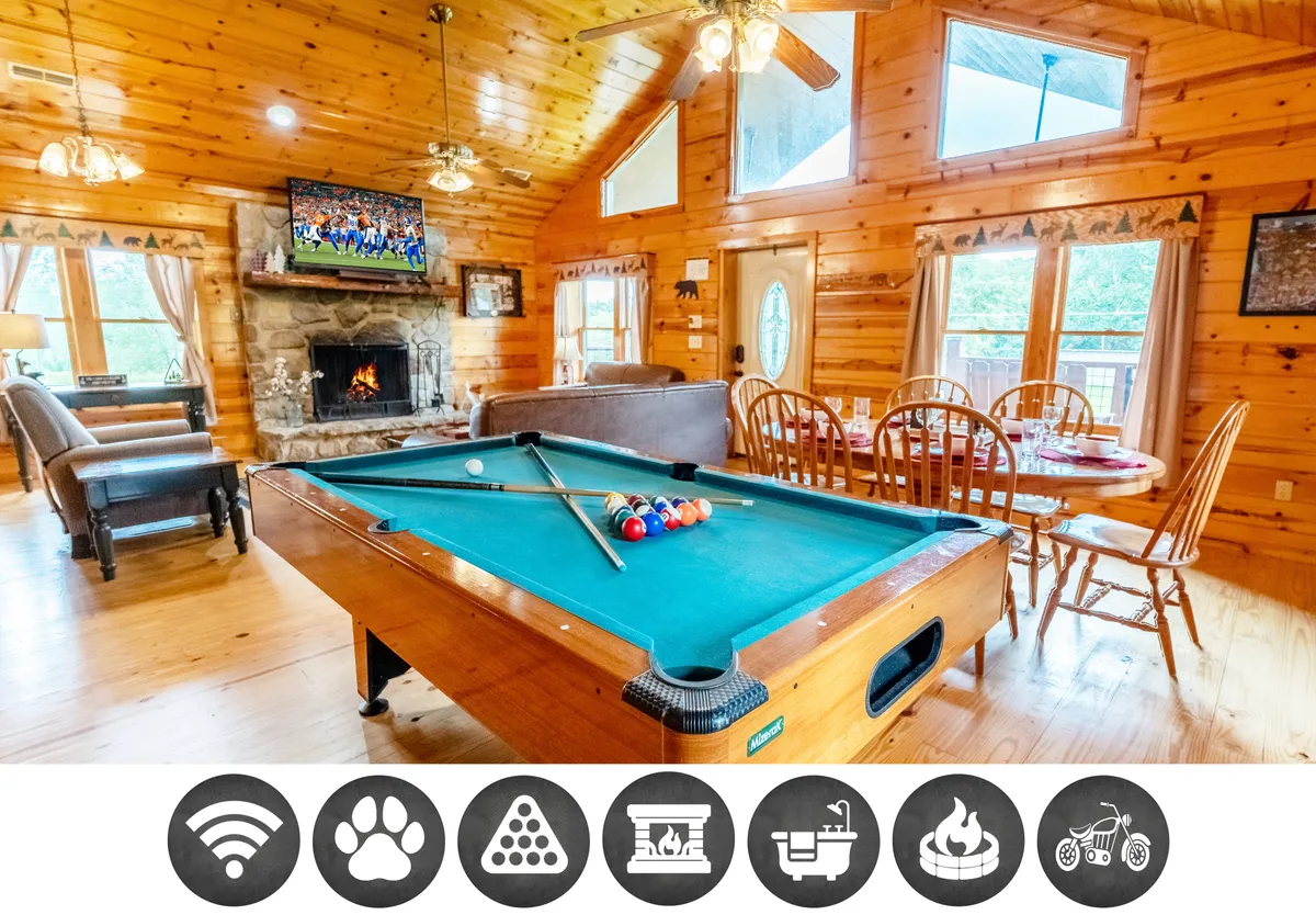 The interior of the cabin features a cozy open-concept living area with a crackling stone fireplace, a pool table ready for friendly games, a spacious dining table for shared meals, a large television, and floor-to-ceiling windows offering a glimpse of the surrounding woods. The space is warm and inviting, designed for families and friends to unwind together.