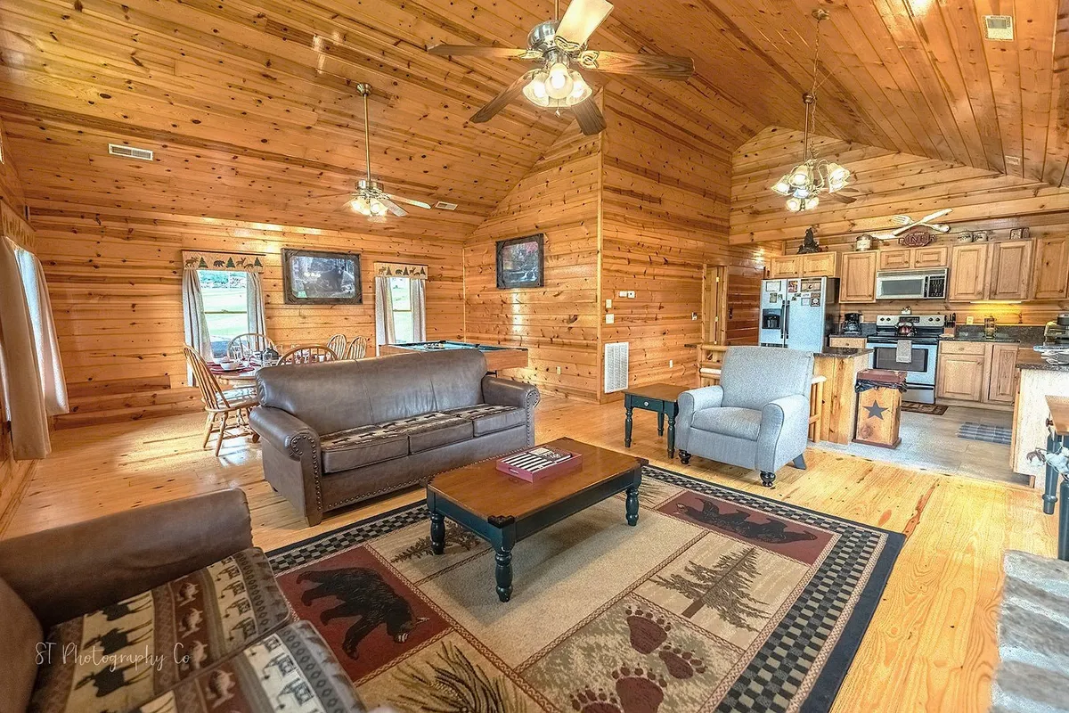A spacious living area with a wooden ceiling, large sofa, coffee table, and a view of the adjacent dining area and kitchen. The warm tones and open layout create a welcoming environment for groups, perfect for relaxing or enjoying game nights together.