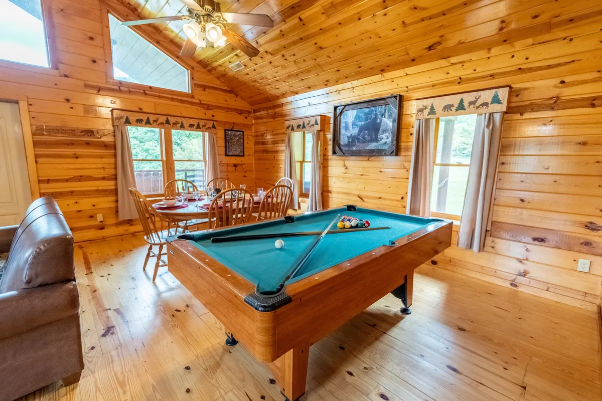 This image captures an open-concept space featuring a pool table and dining area with large windows and wooden walls. The area is filled with light and encourages both fun and social dining experiences.
