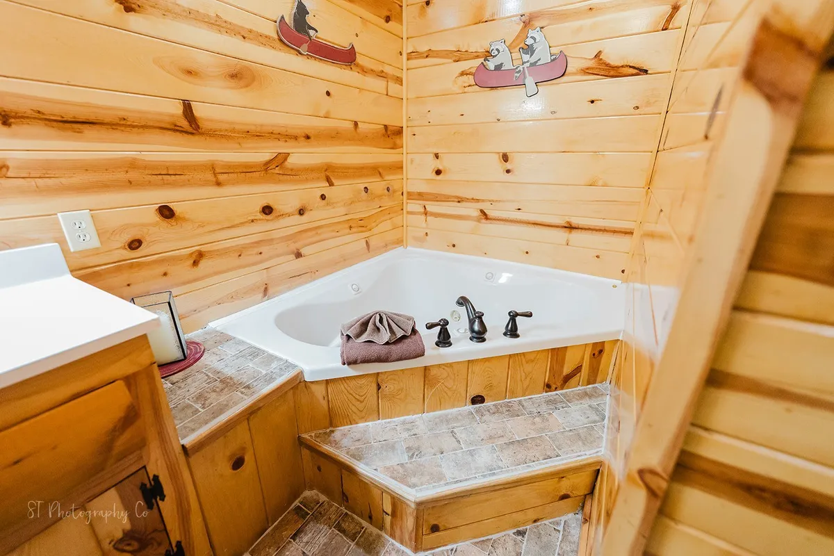 A tranquil bathroom scene featuring a jacuzzi-style jetted tub, wood-paneled walls, and subtle animal motifs, evoking the feel of a mountain retreat's master suite.
